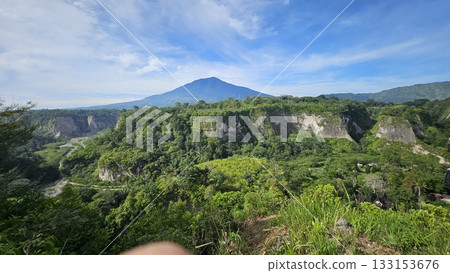 A stunning viewpoint at Panorama Ngarai Sianok showcases lush greenery, towering trees, and a majestic mountain under the clear blue sky, offering a peaceful harmony. 133153676