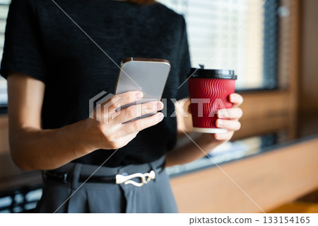 Asian businesswoman holds smartphone and coffee cup in a modern office, showcasing multitasking, digital connectivity Asian businesswoman holds smartphone and coffee cup in a modern office, showcasing multitasking, digital connectivity 133154165