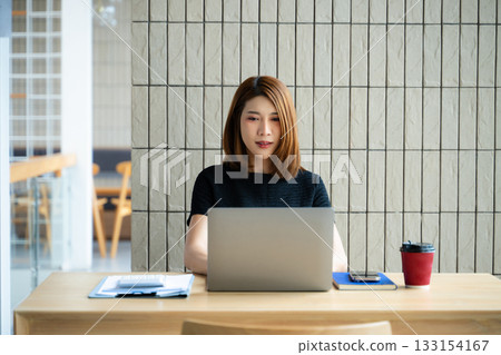 Asian businesswoman on smartphone while reviewing clipboard and laptop in a modern remote office. Asian businesswoman on smartphone while reviewing clipboard and laptop in a modern remote office. 133154167
