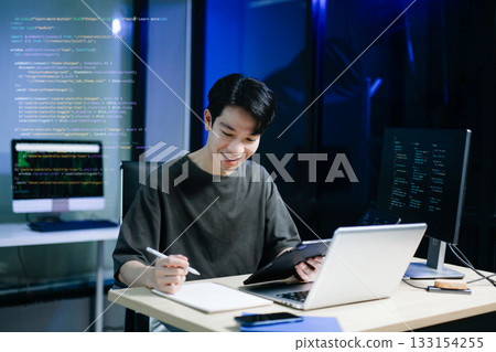 Asian developer writing code at night in modern office setup. Concept of software engineering, programming, digital workspace Asian developer writing code at night in modern office setup. Concept of software engineering, programming, digital workspace 133154255