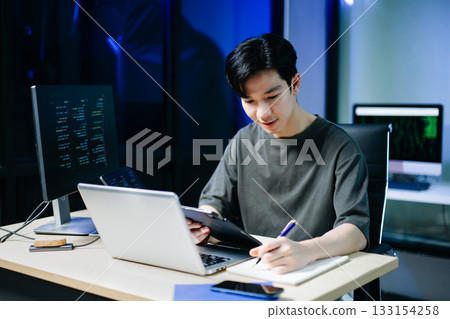 Young male programmer working with tablet and screen displaying code. Modern tech office setup, great for software, coding, IT Young male programmer working with tablet and screen displaying code. Modern tech office setup, great for software, coding, IT 133154258