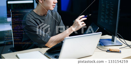 Asian developer writing code at night in modern office setup. Concept of software engineering, programming, digital workspace Asian developer writing code at night in modern office setup. Concept of software engineering, programming, digital workspace 133154259