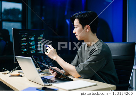 Asian developer writing code at night in modern office setup. Concept of software engineering, programming, digital workspace Asian developer writing code at night in modern office setup. Concept of software engineering, programming, digital workspace 133154260
