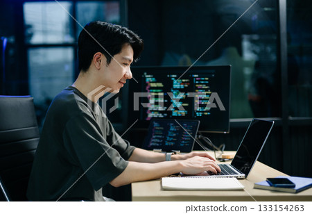 Asian developer writing code at night in modern office setup. Concept of software engineering, programming, digital workspace 133154263
