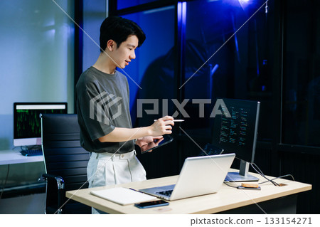 Asian developer writing code at night in modern office setup. Concept of software engineering, programming, digital workspace Asian developer writing code at night in modern office setup. Concept of software engineering, programming, digital workspace 133154271