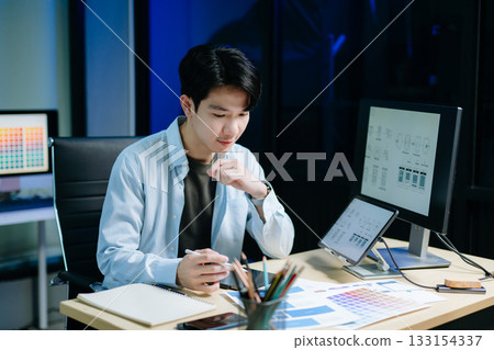 Asian male designer pointing at UX wireframes on screen and tablet in modern office. Ideal for themes in UI UX, digital product design, software 133154337