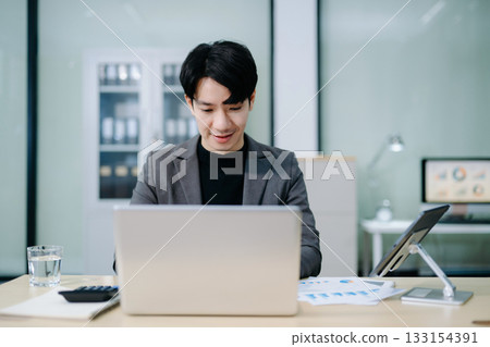 Confident young Asian businessman analyzing financial charts on laptop. Perfect for stock themes in business, finance Confident young Asian businessman analyzing financial charts on laptop. Perfect for stock themes in business, finance 133154391