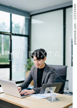 Confident young Asian businessman analyzing financial charts on laptop. Perfect for stock themes in business, finance 133154395