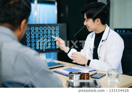 Friendly doctor discussing brain scan results with patient on screen. Health consultation, neurology, diagnosis, and care in clinic Friendly doctor discussing brain scan results with patient on screen. Health consultation, neurology, diagnosis, and care in clinic 133154426