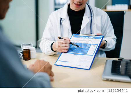 Asian doctor points to a medical form while consulting a patient in a bright clinic office. Concept of health care, insurance 133154441