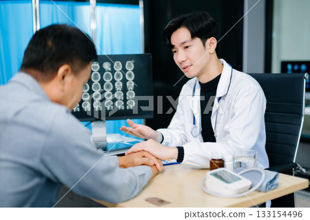 Young Asian doctor shows compassion and explains brain scan results to a patient in a clinic. Concept of medical support, neurology 133154496