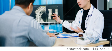 Asian doctor discusses knee X-ray results with senior patient in modern clinic. Concept of orthopedic consultation, bone care, health diagnosis 133154498