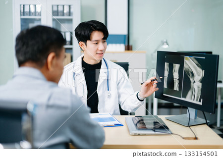 Asian doctor discusses knee X-ray results with senior patient in modern clinic. Concept of orthopedic consultation, bone care, health diagnosis 133154501