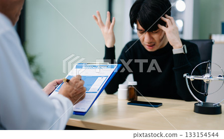 Young Asian man expressing concern in therapy session with psychiatrist. Mental health, stress, support, anxiety, Young Asian man expressing concern in therapy session with psychiatrist. Mental health, stress, support, anxiety, 133154544