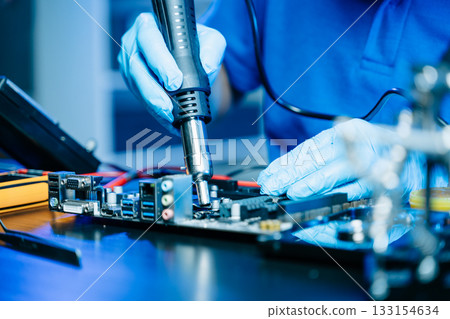Technician in gloves performs precise soldering on circuit board using hot air gun. Concept of electronics repair 133154634