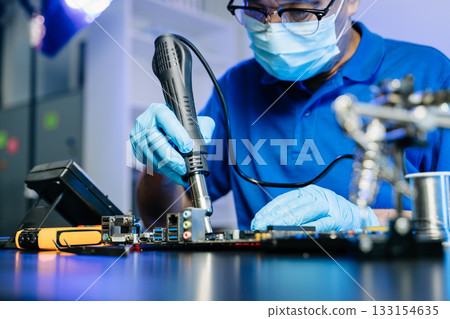 Technician in gloves performs precise soldering on circuit board using hot air gun. Concept of electronics repair 133154635