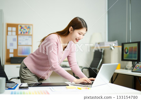 Happy creative designer works with coffee and laptop in modern office, showcasing productivity, style, and professional confidence 133154780