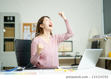 Joyful designer celebrates achievement while using tablet in modern workspace, showcasing creativity, digital success 133154785