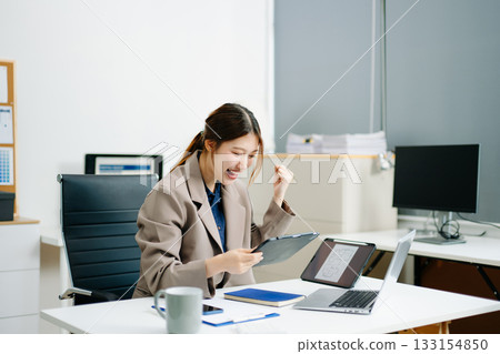 businesswoman celebrating success at her desk with laptop and tablet in a modern office. Perfect for themes of victory, achievement, productivity 133154850