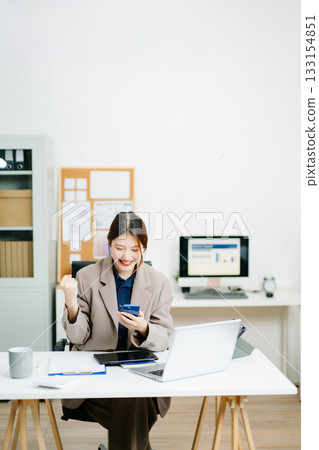 businesswoman celebrating success at her desk with laptop and tablet in a modern office. Perfect for themes of victory, achievement, productivity 133154851