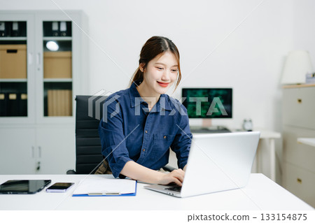 Confident businesswoman working on laptop in a modern office. Elegant and focused, perfect for themes of remote work Confident businesswoman working on laptop in a modern office. Elegant and focused, perfect for themes of remote work 133154875