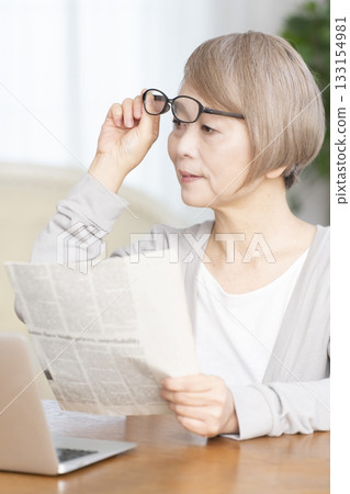 一位老婦人在客廳裡戴著老花眼鏡看報紙。 133154981