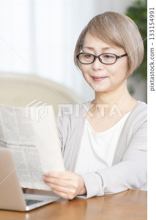 Senior woman reading a newspaper wearing reading glasses in the living room 133154991