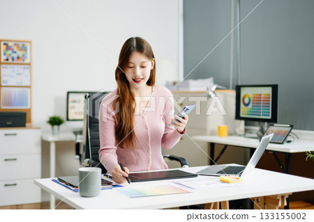 Young female graphic designer using digital tablet and laptop in modern office. Creative workspace, color palettes, and UI UX design Young female graphic designer using digital tablet and laptop in modern office. Creative workspace, color palettes, and UI UX design 133155002