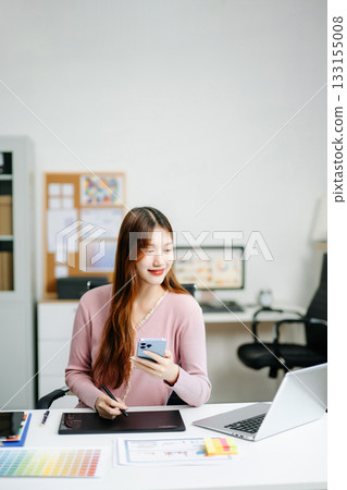 Young female graphic designer using digital tablet and laptop in modern office. Creative workspace, color palettes, and UI UX design Young female graphic designer using digital tablet and laptop in modern office. Creative workspace, color palettes, and UI UX design 133155008