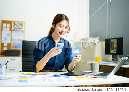 Creative designer stands at her workspace, planning UX/UI with color swatches and wireframes 133155014