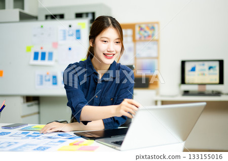 Creative designer stands at her workspace, planning UX/UI with color swatches and wireframes Creative designer stands at her workspace, planning UX/UI with color swatches and wireframes 133155016