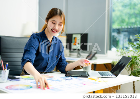 Creative designer stands at her workspace, planning UX/UI with color swatches and wireframes Creative designer stands at her workspace, planning UX/UI with color swatches and wireframes 133155018