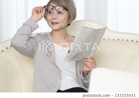 一位老婦人坐在客廳的沙發上,戴著老花眼鏡看報紙。 一位老婦人坐在客廳的沙發上,戴著老花眼鏡看報紙。 133155031