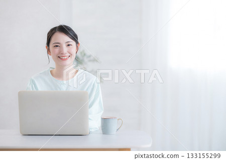 一位微笑的可愛女子在家中或咖啡館使用電腦，看著鏡頭。 133155299