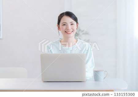 一位微笑的可愛女子在家中或咖啡館使用電腦，看著鏡頭。 133155300