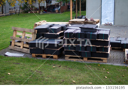 Stacks of black roofing tiles on wooden pallets in a yard during autumn 133156195