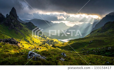 Mysterious scenery of light pouring down on the mountains. Mountain valley illuminated by light shining through the clouds. Mysterious scenery of light pouring down on the mountains. Mountain valley illuminated by light shining through the clouds. 133158417