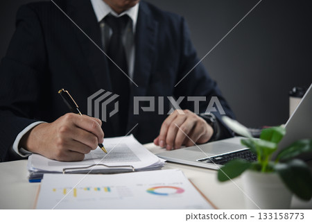 Hands holding pen signing paperwork on desk with laptop, representing contract signing, important decision-making, and corporate governance in a professional office. Hands holding pen signing paperwork on desk with laptop, representing contract signing, important decision-making, and corporate governance in a professional office. 133158773
