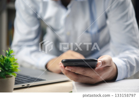 Close-up hand holding smartphone in workplace. Modern corporate lifestyle. Concept of digital communication, remote work, and mobile productivity in modern office. Close-up hand holding smartphone in workplace. Modern corporate lifestyle. Concept of digital communication, remote work, and mobile productivity in modern office. 133158797