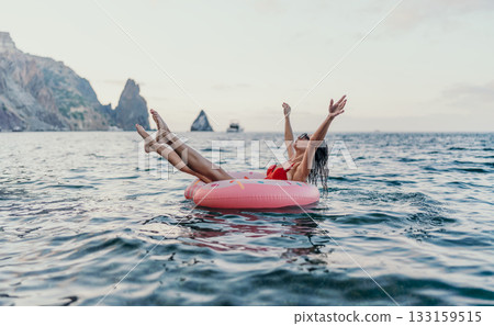 Woman, floating, sea. Happy woman on a pink donut ring in the open sea, enjoying summer vacation by majestic cliffs. 133159515