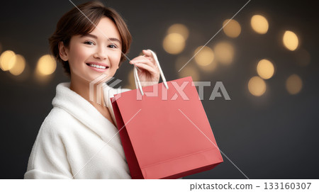 Smiling young woman in cozy white robe holding red shopping bag, surrounded by soft bokeh lights, capturing the joy of shopping experience Smiling young woman in cozy white robe holding red shopping bag, surrounded by soft bokeh lights, capturing the joy of shopping experience 133160307