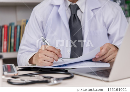 Doctor writing on a medical report at his office. Professional healthcare working on health document, patient's medical history. Medical care, consultation and diagnosis. 133161021