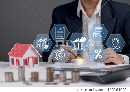 businessman in a suit working on a desk with a model house and icons related to real estate, mortgage, and financial planning. Property in 133161031