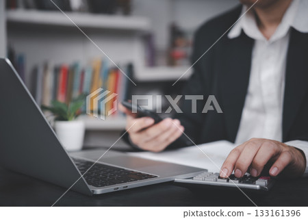 Businessman using calculator and smartphone at desk with laptop, symbolizing financial planning, business accounting, data analysis, modern finance, budgeting, small business management. Businessman using calculator and smartphone at desk with laptop, symbolizing financial planning, business accounting, data analysis, modern finance, budgeting, small business management. 133161396