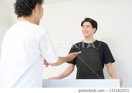 A man wearing an apron serving customers at the reception desk A man wearing an apron serving customers at the reception desk 133162053