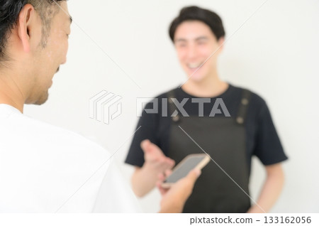 A man wearing an apron serving customers at the reception desk A man wearing an apron serving customers at the reception desk 133162056