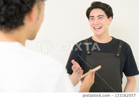 A man wearing an apron serving customers at the reception desk A man wearing an apron serving customers at the reception desk 133162057