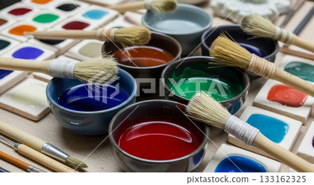 Traditional ceramic bowls filled with vibrant liquid watercolor paints red blue green orange with natural bristle brushes and watercolor palette trays on wooden surface art studio setup Traditional ceramic bowls filled with vibrant liquid watercolor paints red blue green orange with natural bristle brushes and watercolor palette trays on wooden surface art studio setup 133162325