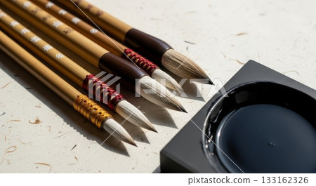 Traditional Chinese calligraphy brushes with bamboo handles and natural bristles arranged beside black ink stone on textured rice paper background 133162326