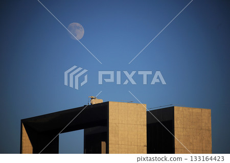 The moon rising above geometric buildings at dusk 133164423